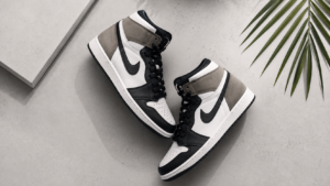 Premium Air Jordan-style sneakers arranged in a clean flat-lay on a light gray minimalist background with soft studio lighting, highlighting the leather texture, stitching, and modern high-top design in a wide commercial banner composition.